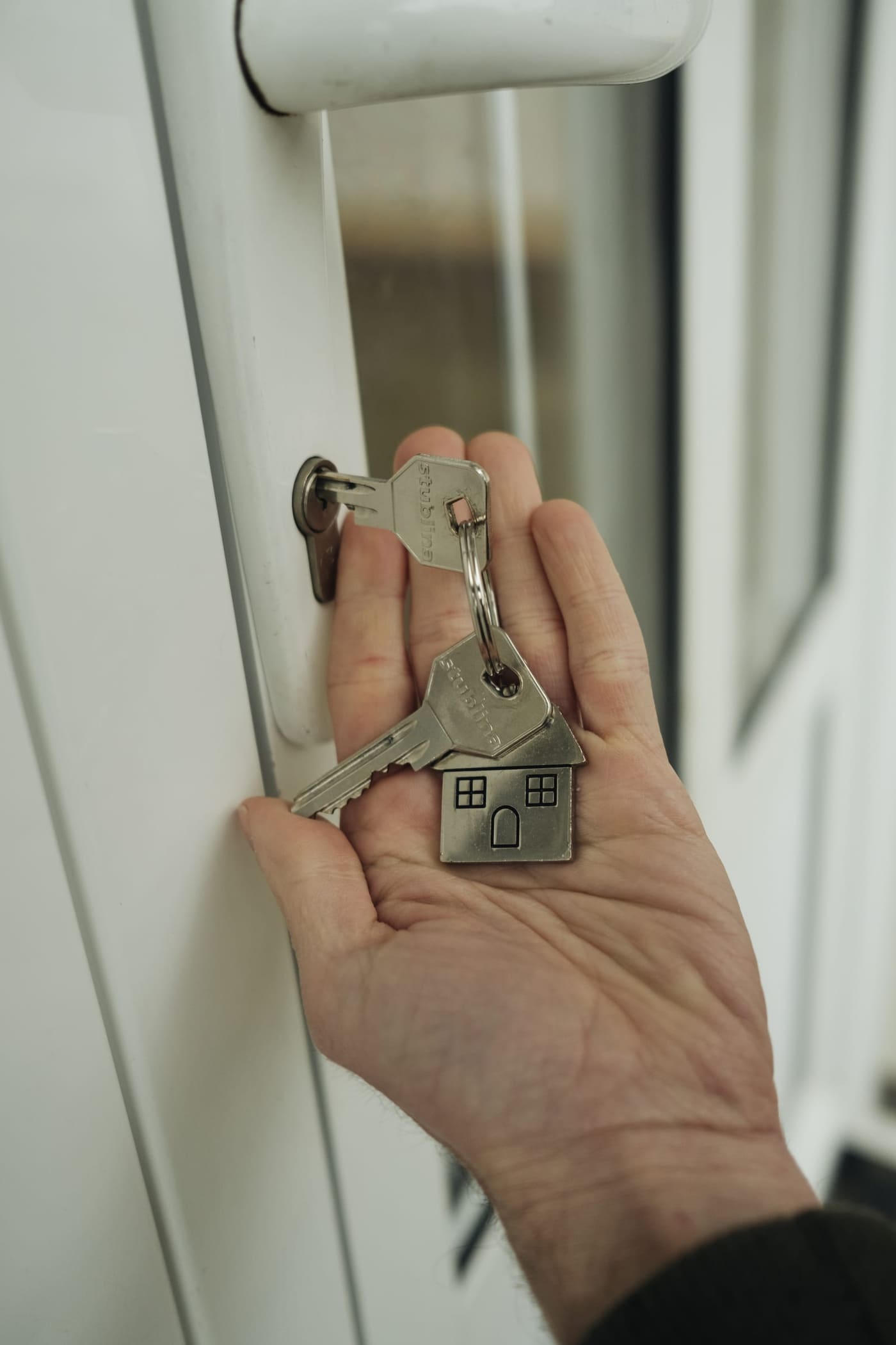 A hand holding house keys with a house-shaped keychain at the front door of a new home